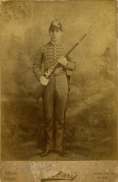 A cabinet card portrait of a young man in full military uniform, holding a weapon.