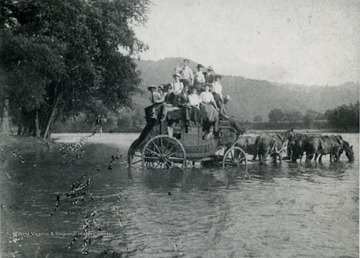 A stage coach stopped at a ford in the river for the horses to drink and the passengers pose for a photograph.