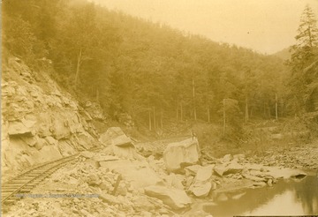 Huge rocks lay along side the track with an unidentified man standing on one boulder in the center of the photograph.
