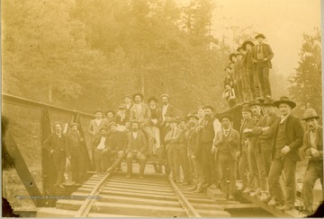 A large group of unidentified people, including civil engineers, survey and construction crews, pose on a railroad bridge. The photograph was taken during the construction of the Ohio extension of the Norfolk &amp; Western Railroad.