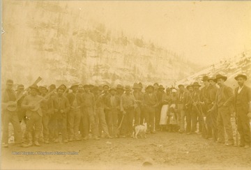 Large group portrait of black and white workers. Some are holding guns, tools or banjos. None are identified.