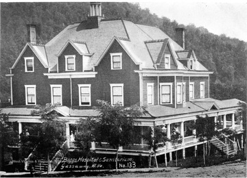 Large three story, clapboard building with a wrap around porch and several unidentified people gathered on the porch, including one woman wearing a white uniform.