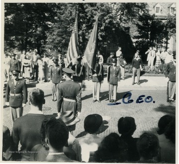 Captain George Barrick Jr., to the right of the flags, stands at attention waiting for General Eisenhower to review Barrick's ROTC Unit on the WVU campus. All other persons in this photograph are unidentified.