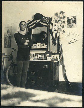 Unidentified student dressed in athletic attire of jersey, shorts and tights, poses a dorm room in Episcopal Hall. Note a bike on one side of the dresser and a gun on the other side.