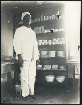 Unidentified African-American man wearing white, stands in a pantry area of the dormitory.
