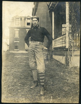 Unidentified WVU student wearing a football uniform poses next to Episcopal Hall on campus. 