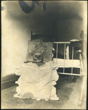 An unidentified human skull with "one" written on its forehead and a cigarette in its mouth, sits patiently on a chair in the dormitory.