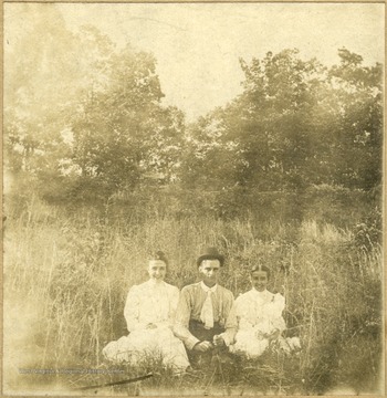 Sitting in the tall grass, Ada Enid Haldeman, Arthur C. Thomas and Olivia L. Haldeman. 