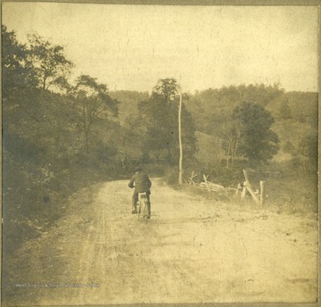 Information included with photograph, "View of Old North Western Pike before it was surfaced, just beyond the 'short turn'". Pictured is Henry Wotney, a friend of Ada Haldeman, riding a wooden bicycle he made. 