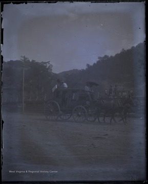 Unidentified driver and passengers ride a stagecoach pulled by a team of horses.