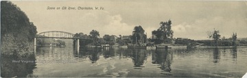 Working boats and barges docked along the shoreline , with a bridge crossing the river in the background.