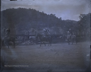 Three unidentified persons dressed as Native Americans ride horses pass a few spectators.