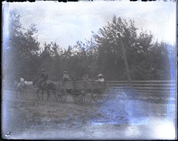 Unidentified mounted rider and passengers in a horse drawn wagon travel down a dirt road.
