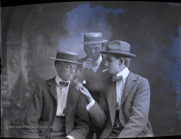 Three unidentified young men, two wearing boater hats, smoke their cigar and cigarettes.