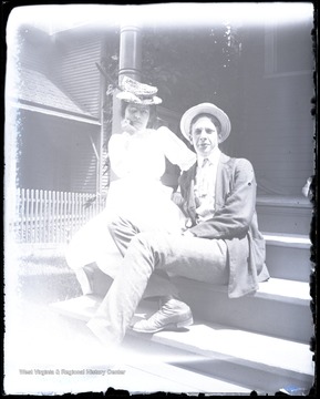 Unidentified man and bespectacled woman pose outside on a stoop.