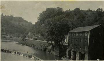 A street car is seen in the background and unidentified people enjoy swimming in the dammed-up mill pond.