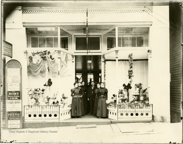 Store employees pose at the front entrance between the display windows exhibiting several fashionable hats.