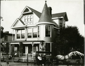 Queen Anne style house with unidentified family sitting on the front porch and two girls sitting a buggy hitched to a horse.