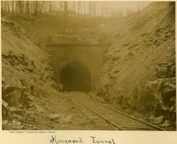 Two unidentified men stand on each side of the tracks at the tunnel entrance.