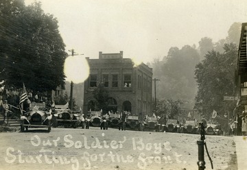 Automobiles, waving American flags line the main street.