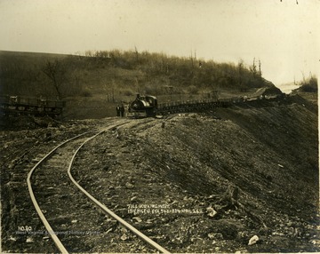 Small engine moves along the track on a filled in area, hauling supplies.