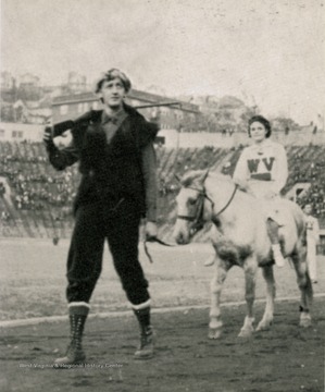 Arnold, the Mountaineer from 1937-1939, leads an unidentified female cheerleader, mounted on a horse around Old Mountaineer Field.