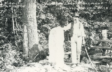 Member of surveying expedition team stands next to the old stone monument marker on the Mason Dixon Line where the state boundary lines of West Virginia, Maryland and Pennsylvania T-intersect.