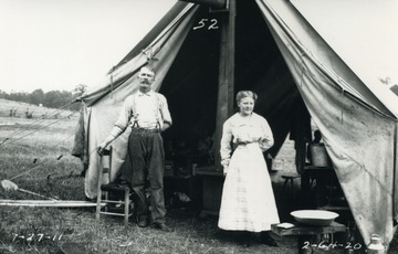 Man and woman stand outside their tent in camp.