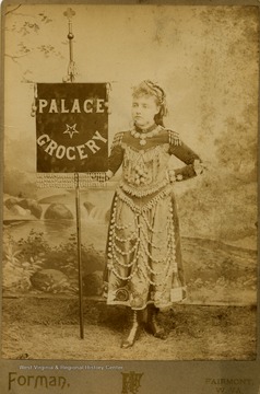 Young girl wearing a costume and holding a banner embossed with words, "Palace Grocery".