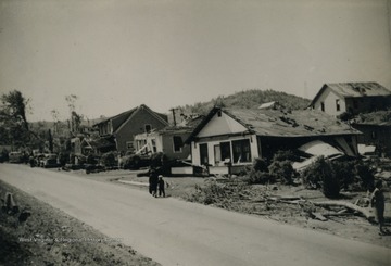 People walk the street observing the damage caused to the homes.