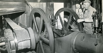 Caption with image published in the "mason-Dixonland Panorama" 1974/12/01, "Grabbing the flywheel, Leslie Neely pulls on it to start the engine."