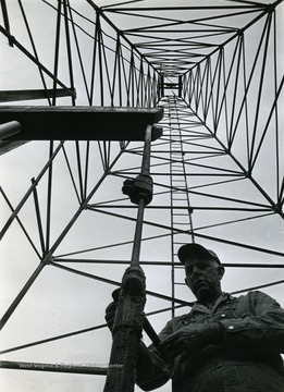 Caption with the image when published in the "Mason-Dixonland Panorama" 1974/12/01, "Pumper Leslie Neely works beneath towering derrick."