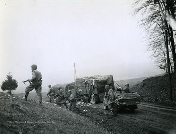 U.S. soldiers move on from a destroyed transport vehicle on the road as one G.I. mans a mounted machine gun in the jeep.