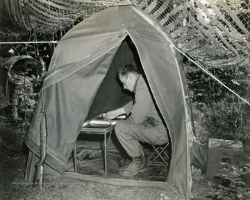 The soldier is most likely Raymond Young, infantry man and combat photographer, United States Third Army. Young is using his tent as a photo lab to develop film while on the front lines.