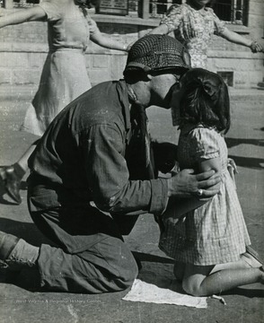 Small girl giving a soldier a kiss on the cheek while women behind them hold hands during the liberation of France in 1944.