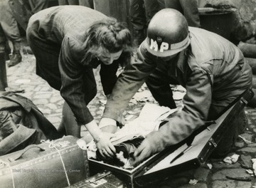 Information on back of photo reads: "Private Thomas H. Olsen of Chicago, Illinois, checks over the baggage brought by one of the German Army women to the prisoner-of-war enclosure of the 83rd Infantry Division, Ninth U.S. Army. The women surrendered after receiving leaflets. Supreme Headquarters Allied Expeditionary Force reported May 1, 1945, that nearly three million German prisoners had been taken by the Allies in the West since "D-Day" (June 6, 1945)."