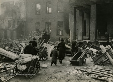 Information on back of photo reads: "Civilians who have returned to captured, war-torn Munchen-Gladbach fill carts with sticks for firewood outside a bomb-shattered broom factory. Munchen-Gladbach, first big industrial city in the Ruhr area to fall to advancing American forces, was taken March 1, 1945, by troops of the Ninth U.S. Army after heavy air and artillery bombardment. It is 10 miles from the Dutch border."