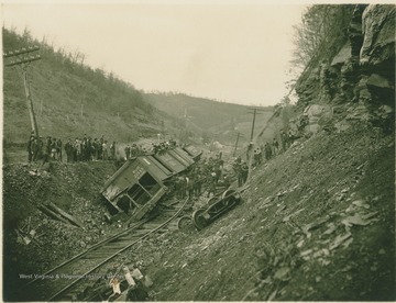 Several curious people inspect the damaged cars of a derailed train.