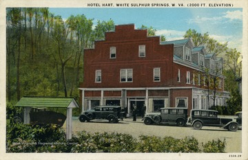 2,000 feet elevation. Hand painted scene of parked cars lining the side of the hotel while a small group of men loiter outside. (From postcard collection legacy system.)