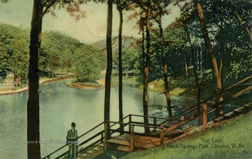 People can be seen boating on the lake in the distance. On the left side of postcard there appears to be a swimming pool and slides. (From postcard collection legacy system.)