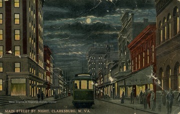 Trolley travels down the middle of the road as people wander the sidewalks at night. (From postcard collection legacy system.)