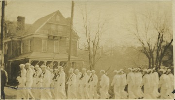 Uniformed military men carrying guns across their shoulders walk down the streets of Morgantown, W. Va.