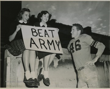 Photo description reads, "West Virginia University Co-Eds, Dot Simons (Lfet) and Maxine Livesay make it plain to backfield star Jim Devonshire that they want their university team to 'Beat Army' in their clash this Saturday, as they visit a practice session at Morgantown, W. Va., Oct. 29."