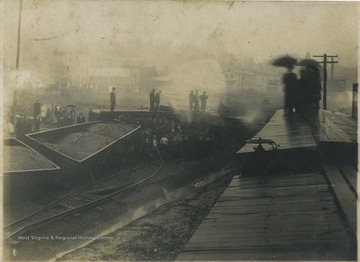 A crowd observes the wreckage of the derailed train. See original for correspondence. 