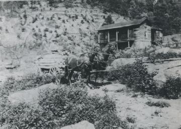 Two horses stand outside of the farm house located in the rocky terrain.