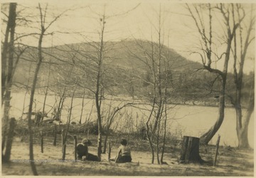 Two unidentified subjects sit by the bank of the river and enjoy the scenery.