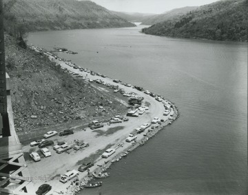 Aerial view of the reservoir shows cars lined along the river that continues on through the mountains in the distance.
