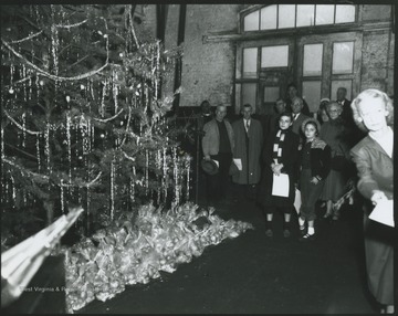 A group of people stand around the large, decorated holiday tree. Subject unidentified. 