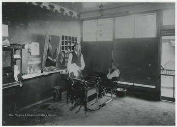 A barber poses by a chair inside the shop.