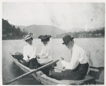 An unidentified man rows two women across the river. Hinton seen in the background to the right. Mrs. R.O. Murrell pictured on the left. 